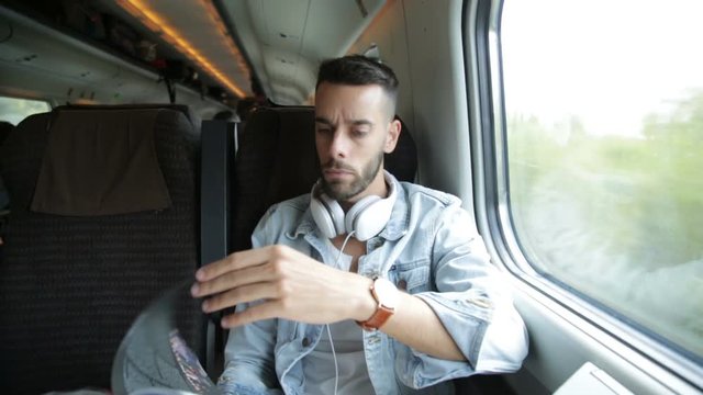 Ragazzo sta viaggiando su un treno mentre ascolta musica dalle cuffie e usa lo smart phone.