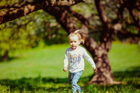 Little girl walks under the trees in a sunny day