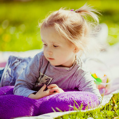 Thoughtuful little girl lies on violet plaid on the lawn