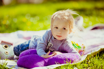 Thoughtuful little girl lies on violet plaid on the lawn