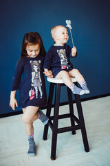 Little sisters sit on a bar chair before blue wall