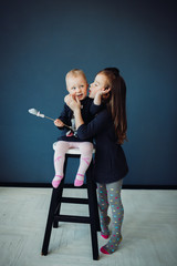 Little sisters sit on a bar chair before blue wall