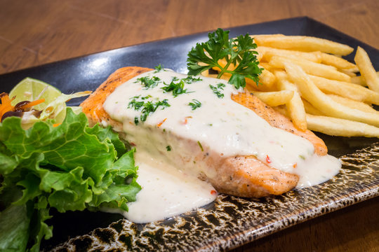 Healthy Grilled Salmon steak, Tartare Cream with salad in a black dish on wood table background for ready to serve.