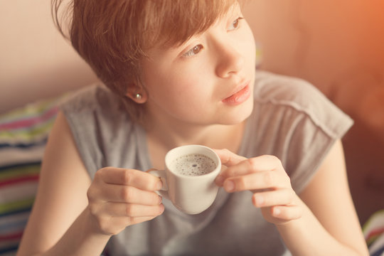 Cute teenager girl lying in bed with a cup of coffee in hand. Toned