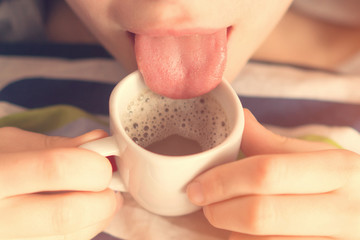 Young girl tries to coffee in a white cup with tongue. Toned