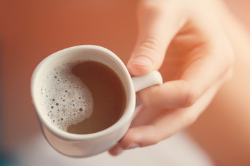 White cup of coffee in hand. Toned