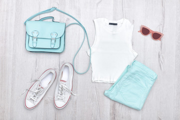 White top, mint-colored jeans, white sneakers and handbag. Fashionable concept. Wooden background.