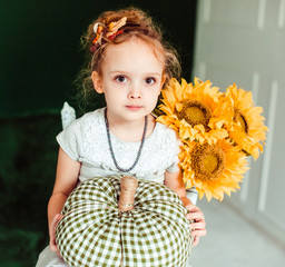 Little girl sits with sunflowers on the chair
