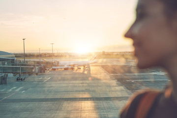 Girl at the airport window looking outside. Focus on the airplane
