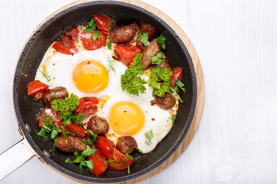 Fried eggs with sausages and vegetables in a frying pan