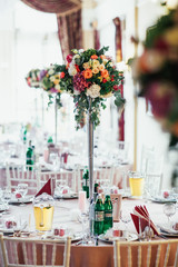 Tall vase with colorful roses stands in the middle of a dinner table