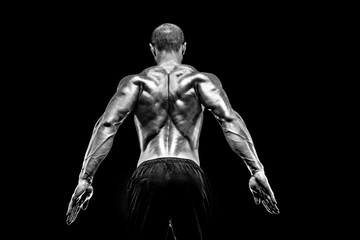 The back view of torso of attractive male body builder on black background.