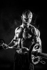 Fototapeta na wymiar Studio portrait of topless bodybuilder performing biceps exercise with concentrated face over black background with smoke and light. Cutout.