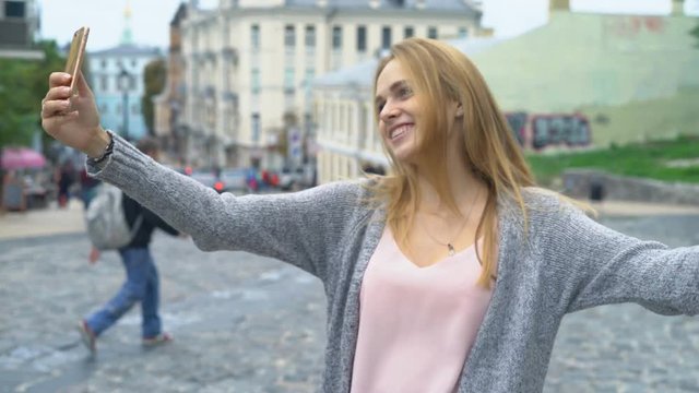 young attractive tourist girl walks around the old city. Narrow streets with beautiful colored houses. happy woman smiles into the camera and winks. the girl is dressed in a gray gray cardigan and