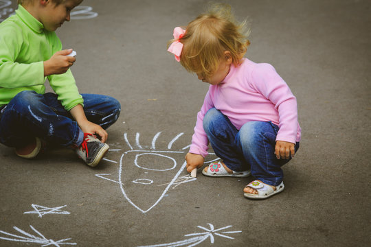 little boy and girl drawing with chalk on asphalt