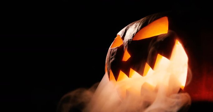 Scary carved halloween pumpkin in hot burning hell fire flames. The big helloween pumpkin has a mad face with glowing eyes and also a smoke in its mouth and teeth.