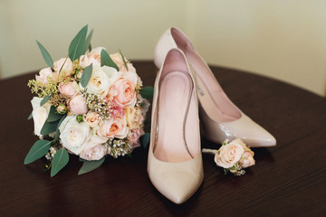 Beige shoes stand on the wooden table with a wedding bouquet