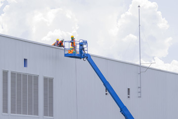 Workers in a baskets are installing sheet, building a factory.