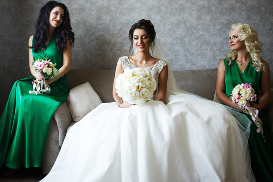 Bride And Bridesmaids In Green Dresses Sit On Grey Sofa In The Room