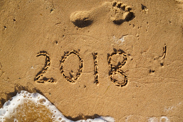 New Year is coming concept - 2018 written on a beach sand with wave of the sea