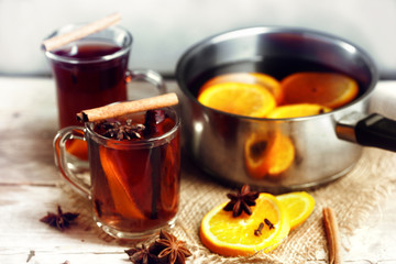 mulled wine in a glass mugs and in a pot with Christmas spices like orange slices, cloves, star anise and cinnamon on a bright rustic wooden tabled