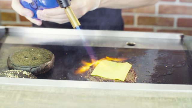 Hands of chef burning a burger with an open flame