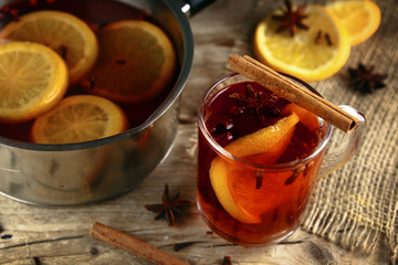 mulled wine in a glass mug and in a pot with Christmas spices like orange slices, cloves, star anise and cinnamon on a rustic wooden table