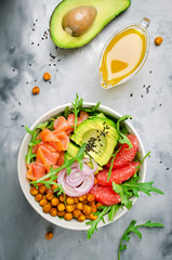 Healthy salad bowl with salmon, grapefruit, spicy chickpeas, avocado, red onion and arugula