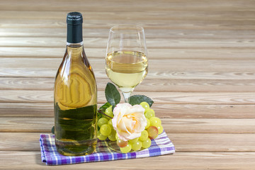 Bottle and glass of white wine are stand on table together with rose