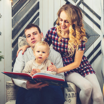 Portrait of young family: mom, dad and little son. All of them sitting in decorated room, farher holding a childrens book. Concept of Merry Christmas and New Year