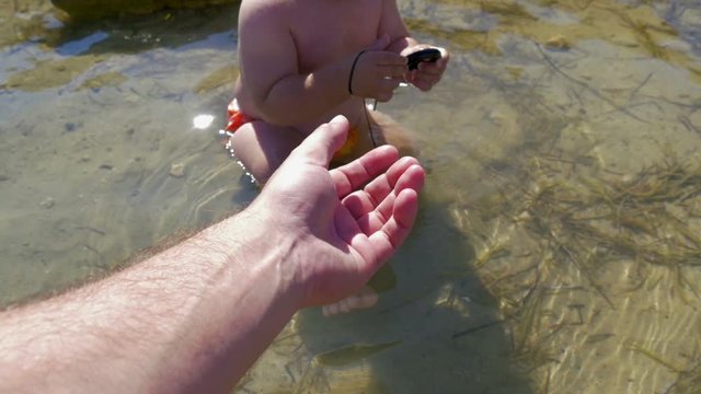 baby boy found some rubber garbage in shallow sea and refuses to give it to dady. in slow-motion hd