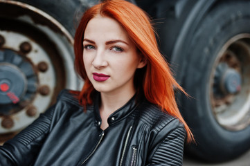 Obraz na płótnie Canvas Red haired stylish girl wear in black, sitting against large truck wheels.