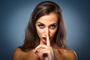 people, silence, secret, gesture and beauty concept - beautiful young woman holding finger on lips over blue background