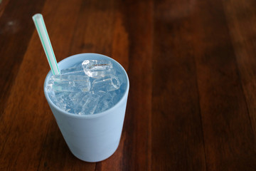 Ice in plastic glass with straw on wood table background.