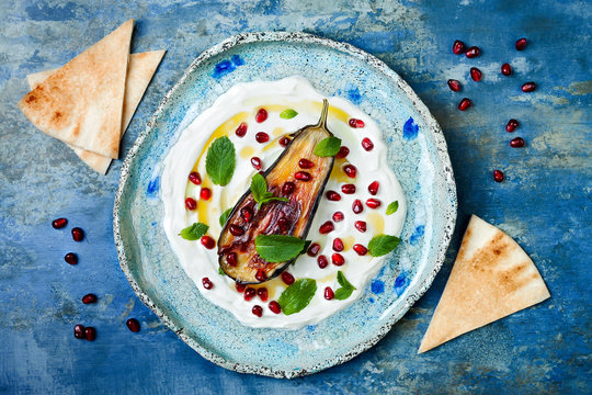 Labneh middle eastern lebanese cream cheese dip with roasted aubergine, pomegranate, mint and pita. Top view, overhead