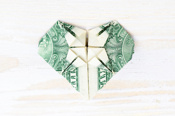 Close-up of origami heart of banknote. Origami made of a dollar bill on light wooden background, copyspace for text