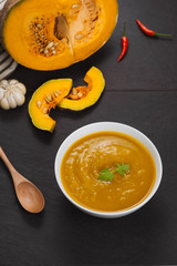 Bowl of pumpkin soup on black stone background.