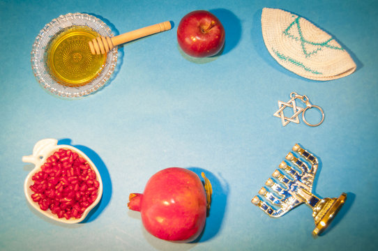 The Jewish New Year Rosh Hashanah concept - apple shaped plate with red pomegranate seeds, plate with honey, apples and David Star on a blue background. Rosh Hashanah greeting