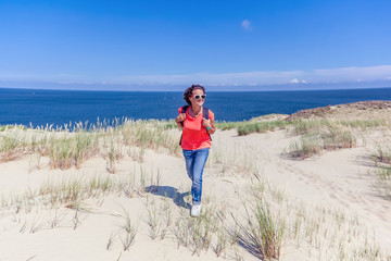 Beautiful young woman traveler with a backpack on the background of the sea and white dunes