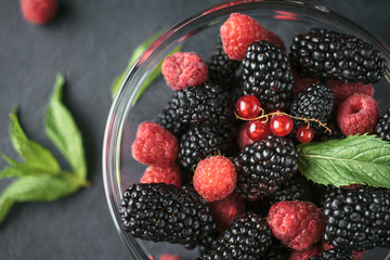 Top view photo of a glass plate with ripe red blackberries, raspberries and green mint leaves on a black surface. Macro photo of ripe blackberries and raspberries.
