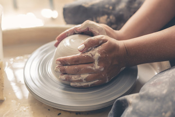 Potter works with white clay on pottery wheel