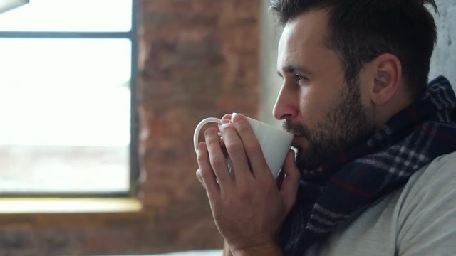Scaled up of relaxed millennial guy in scarf drinking tea