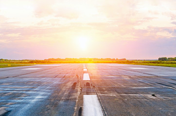 Airport runway airplanes with traces of rubber tires at dawn in the morning with sun glare