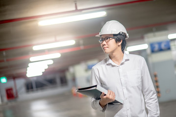 Young Asian Engineer or Architect holding files while wearing personal protective equipment safety helmet at construction site. Engineering, Architecture and building construction concepts