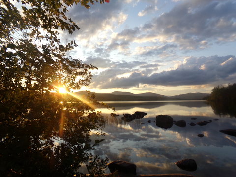 Sunset behind mountains, reflecting off lake, with colorful, cloudy sky. Wester Maine, September,  2017.