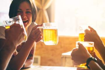 Friends toasting with glasses of light beer at the pub. Beautiful background of the Oktoberfest. A group of young people while relaxing at the bar. fine grain. Soft focus. Shallow DOF