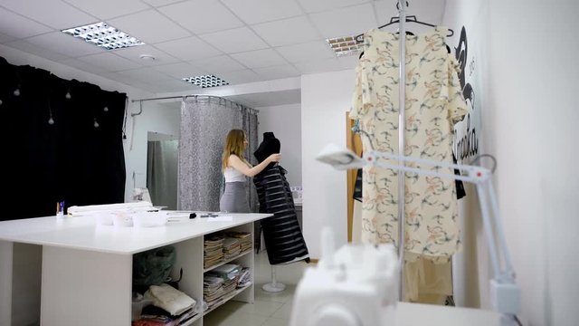 Fashion designer in casual clothes is making measurements of dress using mannequin in dressmaking workshop. Image of female couturier in atelier holding black cloth and creating design of future gown.