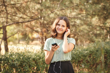 Pretty teenage girl outdoors looking at camera and smiling. Beautiful girl with headphones listening to music in the park.