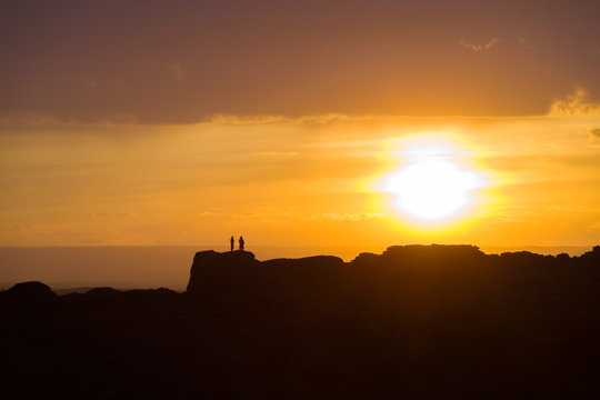 Two People On Distant Ridge Sunset Orange Sky