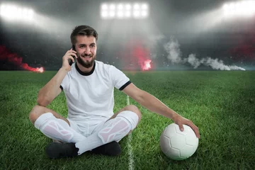Papier Peint photo Foot Fußballer sitzt nach gewonnenen Spiel auf dem Rasen und telefoniert